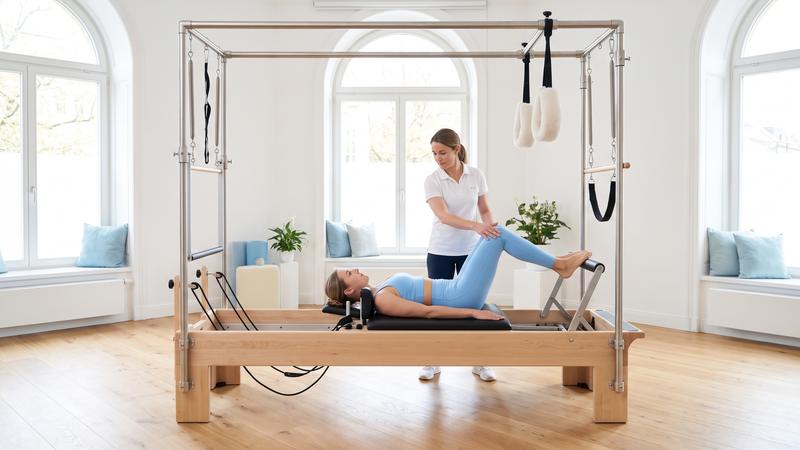 Fizyoterapist eşliğinde kule çerçeveli cadillac reformer aletinde footwork egzersizi yapan danışan